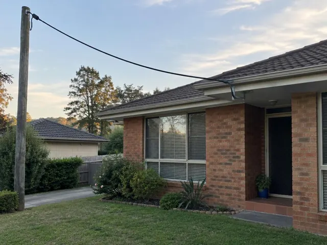 Overhead service cable and bracket on a brick house exterior in Belmont