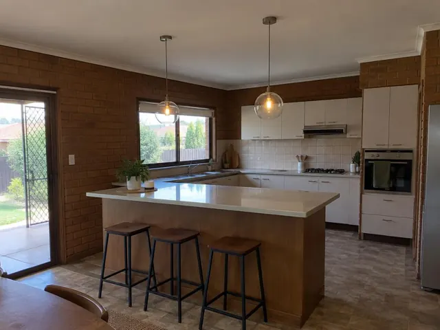 Kitchen with two glass pendant lights over an island, brick walls and white cabinets in Belmont